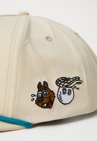 Beige caps med broderte tegnefilm hunder og golfball design, med en lys blå aksent. Glatt stoff med en strukturert form.