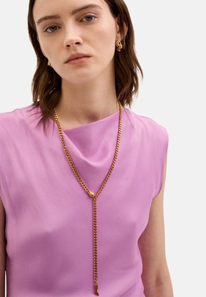 Blusa rosa con scollatura drappeggiata, abbinata a una lunga collana d'oro con finitura texture. Orecchini in una tonalità d'oro simile.