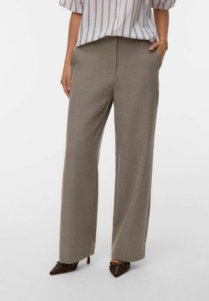 Vrouw in beige wijdlootbroek, gestreept button-up shirt en bruin puntig hakken met decoratieve lussen en strikken.