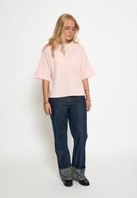 Rozā pūkaina blūze ar īsām piedurknēm un apaļu dekoltē, kombinēta ar tumšiem denimu platām biksēm ar salocītu apakšmalu. Melni potītes zābaki.