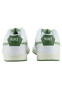 Weiße Sneaker mit grünen Akzenten, ausgestattet mit einem gepolsterten Schaft, strukturiertem Rückenteil und Nike-Branding an der Fersenlasche. Gummisohle sichtbar.