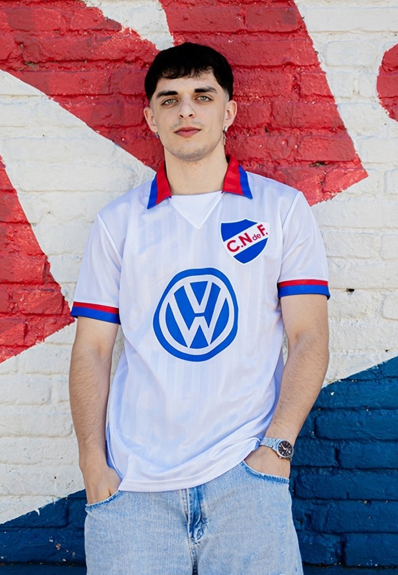 Witte trui met verticale strepen, rode en blauwe accenten, met een groot blauw Volkswagen-logo en schildembleem met de tekst "C.N. de F."