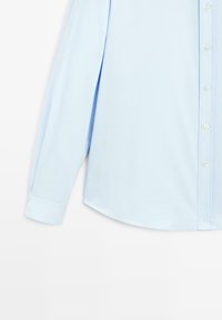 Camicia a maniche lunghe blu chiaro con chiusura a bottoni, colletto a punta, orlo arrotondato e superficie in cotone liscio. Design semplice, senza motivi.