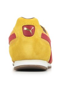 Sneaker in suede giallo con accenti rossi, dotato di collare imbottito, logo dorato e suola intermedia bianca. Cuciture dettagliate sul tallone.