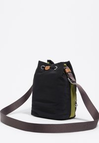 Czarna torba materiałowa ze ściągaczem, z oliwkowozielonym bocznym panelem i długim szarym paskiem, rozłożona na białej powierzchni.