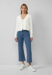 Witte gebreide cardigan met een V-hals en een enkele knop, gecombineerd met lichtblauwe flared jeans en witte sneakers. Soepele textuur, ontspannen pasvorm.