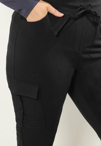 Czarne spodnie cargo z elastycznym pasem na sznurki, kieszenią boczną oraz miękkim, rozciągliwym materiałem idealnym do codziennego użytku.