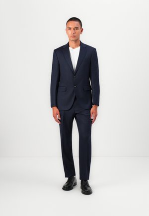 Navy two-piece suit featuring a tailored blazer with notch lapels and flat-front trousers. Worn with a white crew-neck T-shirt and black shoes.
