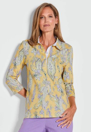 Chemise jaune à col avec un motif floral paisley, manches trois quarts et col blanc. Tissu doux avec une texture légère.