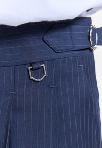 Pantalon bleu marine à fines rayures avec une ceinture assortie dotée d'une boucle rectangulaire argentée et d'un détail anneau en D près de la taille.