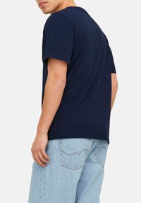 Marineblaue Baumwoll-T-Shirt mit kurzen Ärmeln und Rundhalsausschnitt, getragen von einer Person in hellblauen Jeans.