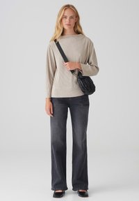 Beige geripptes Oberteil mit langen Ärmeln, kombiniert mit dunklen Schlagjeans. Eine kleine schwarze gesteppte Umhängetasche rundet das Outfit ab.