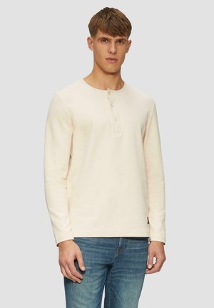 Langarm, lichtroze henleyshirt gemaakt van textielstof met een knoopsluiting van drie knopen en een ronde kraag, gecombineerd met blauwe jeans.