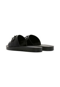 Sandalias de slide negras con una parte superior sintética suave que presenta un detalle decorativo en forma de lazo. Suela plana con superficie texturizada para mayor agarre.