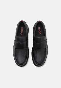 Black leather loafers with a smooth surface, rounded toe, and cushioned insole. Features a stitched detailing and a raised strap across the vamp.