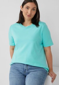 Turkooise t-shirt met korte mouwen, gemaakt van zachte stof, met een ronde halslijn en een relaxte pasvorm, gecombineerd met lichtblauwe spijkerbroek.