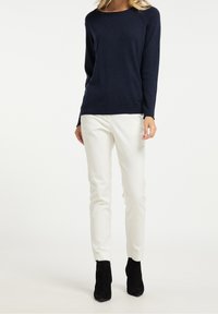 Marineblauer Pullover mit langen Ärmeln aus weichem Material, kombiniert mit weißen Slim-Fit-Hosen und schwarzen Stiefeletten, die ein einfaches und tailliertes Design zeigen.