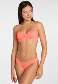 Costume da bagno corallo con top bandeau a twist e spalline regolabili. I slip presentano arricciature laterali e un piccolo accento metallico sull'anca.