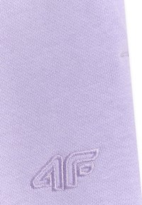 Gros plan sur un tissu lavande avec un logo "4F" brodé en relief dans un fil assorti près du coin inférieur droit.