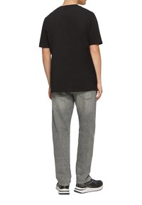 T-shirt en coton noir à manches courtes, associé à un jean en denim gris clair, au fit décontracté et au design à cinq poches, porté avec des baskets noires.