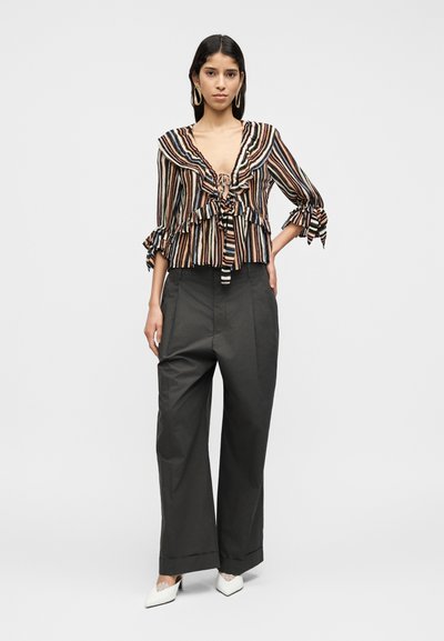 Ριγέ πολύχρωμο τοπ από ελαφρύ ύφασμα με βολάν και κόμπο μπροστά, συνδυασμένο με ψηλόμεσο γκρι παντελόνι φαρδιάς γραμμής και λευκά παπούτσια.