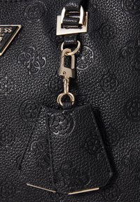 Sort taske lavet af tekstureret læder med præget mønster og en lås i gyldent metal. Inkluderer en aftagelig lædermærkat.