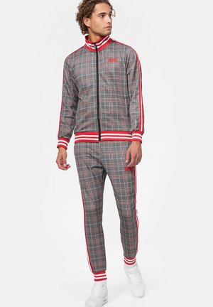 Grijze geruite trainingspak met rode accenten en strepen, zip-up jack met hoge kraag en aansluitende broek met elastische boorden. Geweven stof.