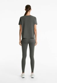 Tricou sportiv de culoare verde închis și colanți, având o textură netedă și o croială lejeră, asortați cu încălțăminte sport de culoare deschisă.