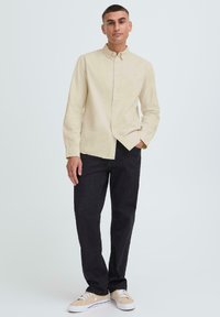 Camisa de botones de color beige claro con cuello, combinada con pantalones negros de corte holgado y zapatillas beige. Tela suave, diseño simple, sin patrones.