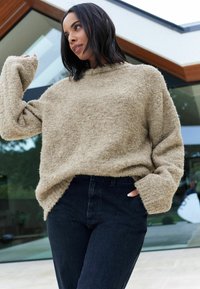 Beige, texturerad tröja med hög hals och oversized passform, kombinerad med högmidjade svarta jeans. Avslappnad, lugn stil.