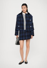 Mørkeblå og sort rutet cropped jakke med store sølvknapper, parret med en grå sweater og matchende nederdel, mens hun holder en grå clutch.