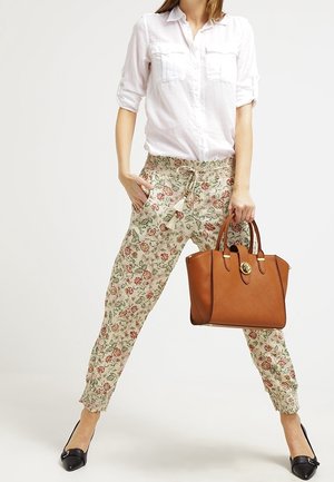 Brązowa skórzana torba o teksturowanym wykończeniu, złote akcesoria, spodnie w kwiatowy wzór oraz biała koszula z guzikami, zestawione z czarnymi balerinami.