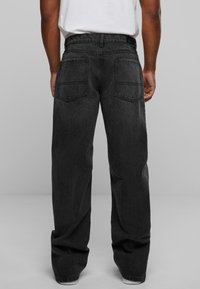 Black denim jeans with a loose fit, featuring double back pockets and a waistband. Texture is smooth, with stitching visible along seams.
