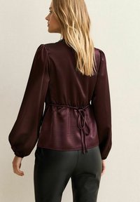 Burgundy satinblus med långa puffärmar, dragsko i midjan och mjuk textur. Kombinerad med åtsittande svarta byxor som visar upp en slank design.