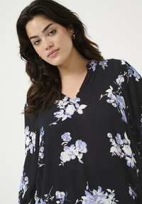 Zwarte blouse met een bloemenpatroon in blauw en wit. V-halsontwerp met losse mouwen en een gestructureerde stof.