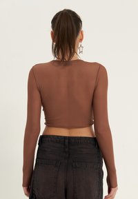 Brun långärmad crop-top i genomskinligt material, matchad med mörka denimbyxor med hög midja, bakfickor och en blekt finish.