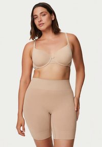 Sujetador sin costuras color nude con tirantes ajustables y aro, combinado con pantalones cortos compresivos de cintura alta en color nude, con textura suave y sin costuras visibles.