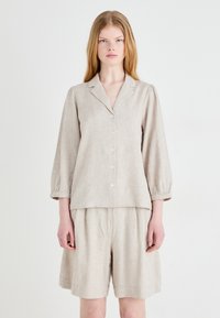Blusa in lino beige con bottone frontale, colletto a scollo a V e maniche a palloncino, abbinata a pantaloni corti larghi coordinati.