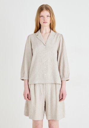 Blusa in lino beige con bottone frontale, colletto a scollo a V e maniche a palloncino, abbinata a pantaloni corti larghi coordinati.