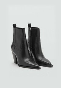 Botas de tobillo de cuero negro con punta afilada, tacón alto, cremallera lateral y diseño con tira para tirar. Textura suave y detalles de costura mínimos.