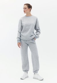 Grå sweatshirt og matchende sweatpants lavet af blødt stof; har elastiske manchetter og en afslappet pasform. Båret med hvide sneakers.