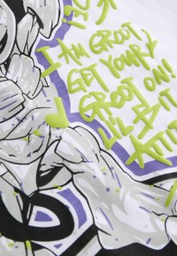 Bílá látka s grafickým potiskem zobrazeným karikaturou. Text jasně zelené barvy zní: "JSEM GROOT, DOSTAŇTE SVÉ GROOOT NA! MALÁ TROCHA POSTOJU!"