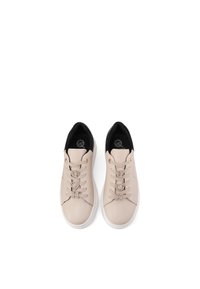 Sneakers in pelle sintetica beige con accenti neri, dotati di occhielli decorativi simili a gioielli e una suola piatta bianca. Texture liscia in tutto il modello.
