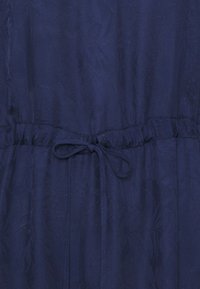 Prenda de color azul marino con un tejido texturizado, cintura elástica con un cordón ajustable y un patrón floral en la superficie.