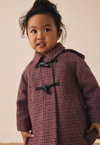 Manteau caban à carreaux roses et noirs avec capuche, doté de fermetures à boutons à bascule et de poches latérales. Texture douce et forme structurée.