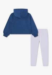 Modrá krátká mikina s kapucí a dlouhými rukávy, zkombinovaná s bílými legínami. Oba kousky jsou vyrobené z hladké, měkké látky s elastickým pasem.