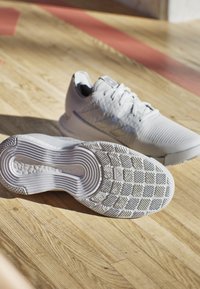 Scarpe da ginnastica bianche con una tomaia testurizzata e una suola liscia, dotate di una suola in gomma con motivo e design a tre strisce sul lato.