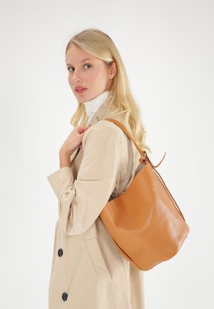 Braune Leder-Eimerhandtasche mit strukturierten Oberfläche, lässiger Form und einem einzelnen Schultergurt. Vor einem hellen Hintergrund.