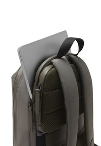 Sac à dos pour ordinateur portable en vert olive, doté de compartiments rembourrés, d'accents en maille texturée et de deux zips. Ordinateur portable partiellement visible.