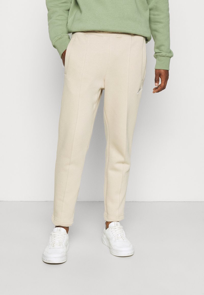 Beiga tapered sweatpants med sidofickor och textilstruktur. Bärs med en grön sweatshirt och vita sneakers.